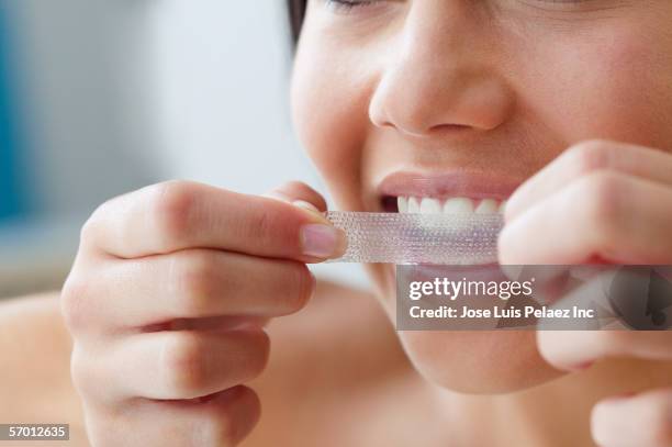 close up of young woman using a teeth whitening strip - sbiancamento dentale foto e immagini stock