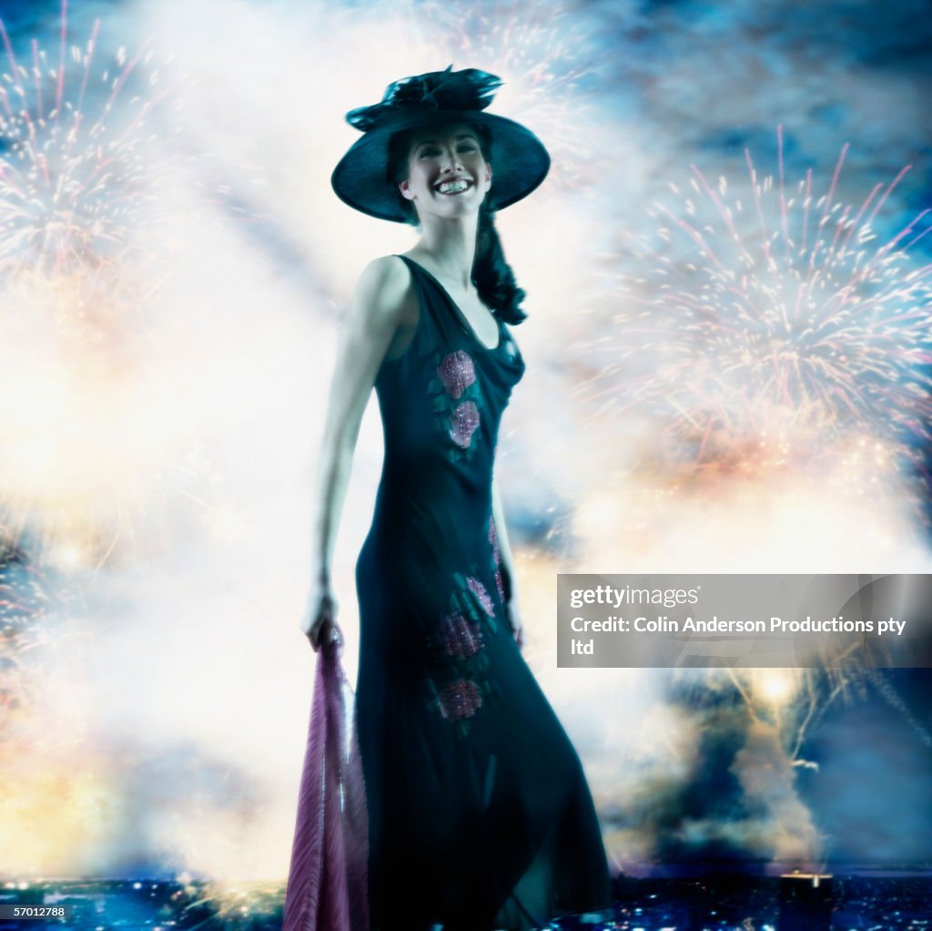 Young woman in fancy dress smiling as fireworks explode behind her