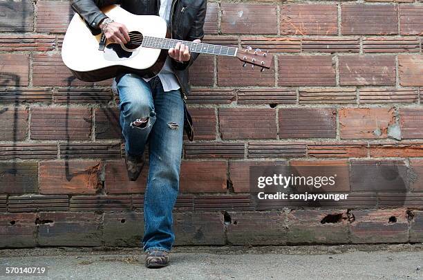 man in leather jacket and cowboy boots playing the guitar in an alley - street musician stock pictures, royalty-free photos & images