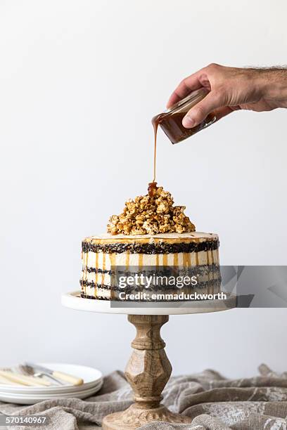 man's hand pouring caramel on a chocolate sponge and buttercream cake - cakestand stock-fotos und bilder