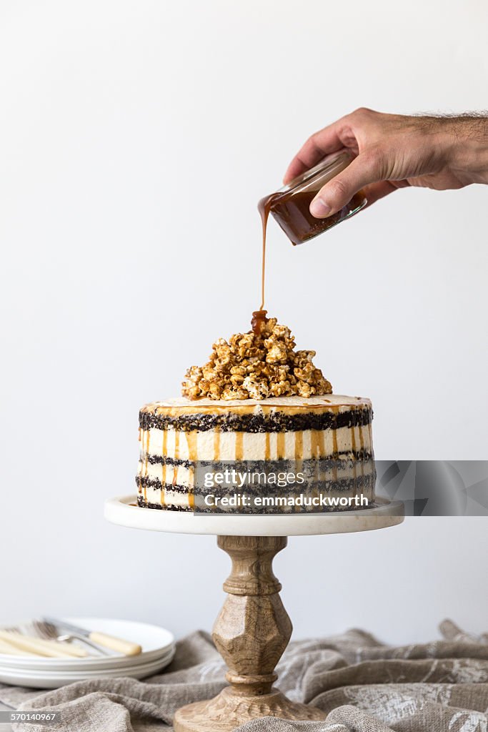 Man's hand pouring caramel on a Chocolate sponge and buttercream cake