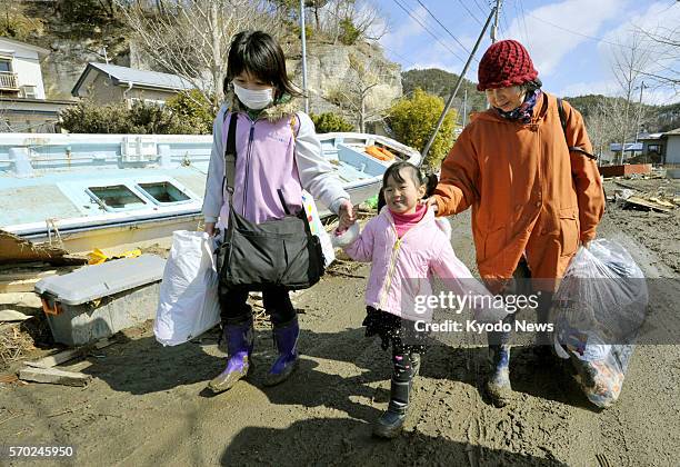 Japan - Members of a family fetch clothing from their ruined home in tsunami-hit Higashimatsushima, Miyagi Prefecture, on March 18 a week after the...