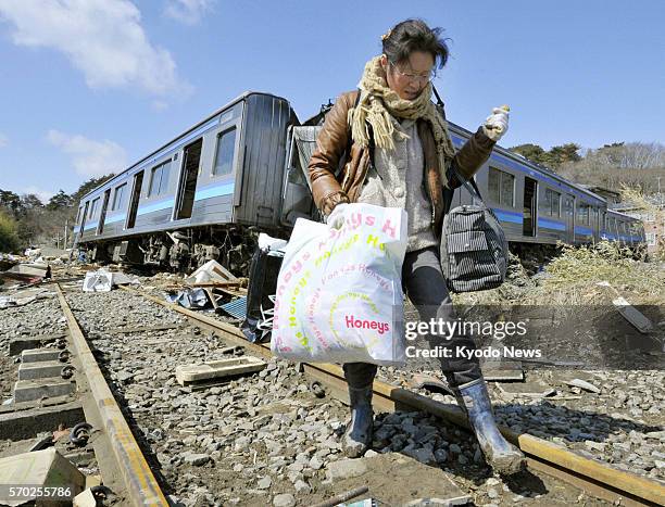 Japan - A woman carrying a bag of clothing, which she retrieved from her tsunami-hit home, walks on a rail track, past a derailed train on the JR...