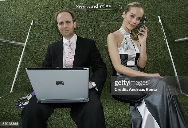 Model uses her mobile phone as a man works on his lapop at the CeBIT computer fair in the northern German town on March 8, 2006 in Hanover, Germany....