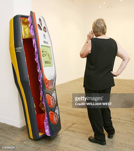 Woman speaks on a phone next to a coffin carved in the shape of a mobile phone by the Paa Joe Carpentry workshop in Ghana and commissioned for...