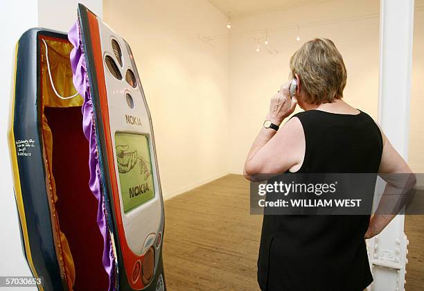 Woman speaks on a phone next to a coffin carved in the shape of a mobile phone by the Paa Joe Carpentry workshop in Ghana and commissioned for...