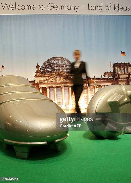 Fair hostess walks past giant mockups of football shoes in front of a poster of Berlin's Reichstag building at the booth of the initiative "Germany -...