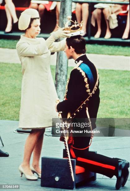 The Investiture of The Prince of Wales at Caernarvon Castle on July 1, 1969. Prince Charles kneels before the HRH Queen Elizabeth II as she places...