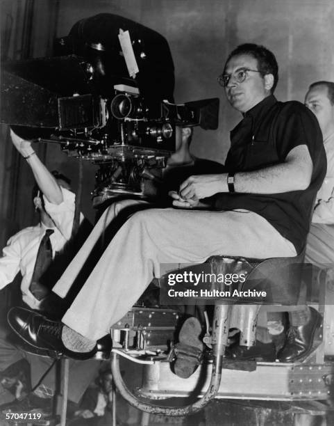 American playwright, screenwriter, and director Clifford Odets , dressed in a short sleeve shirt and eye glasses, sits behind a movie camera and...