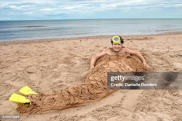 boy buried in sand sculpted to look like a merman - buried stock-fotos und bilder