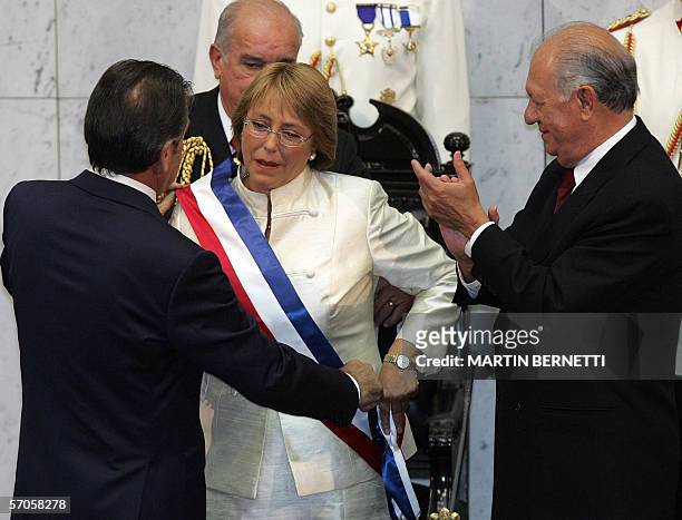 Chilean President Michell Bachelet is helped with the sash by former President Eduardo Frei while outgoing President Ricardo Lagos applauds, during...