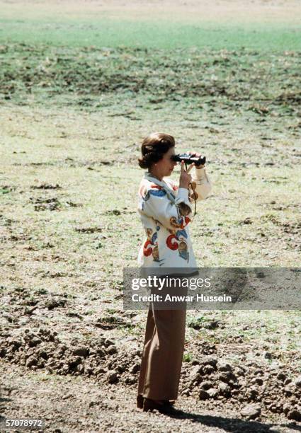 Queen Elizabeth II watches the wildlife through a pair of binoculars while on Safari in Zambia in 1979.