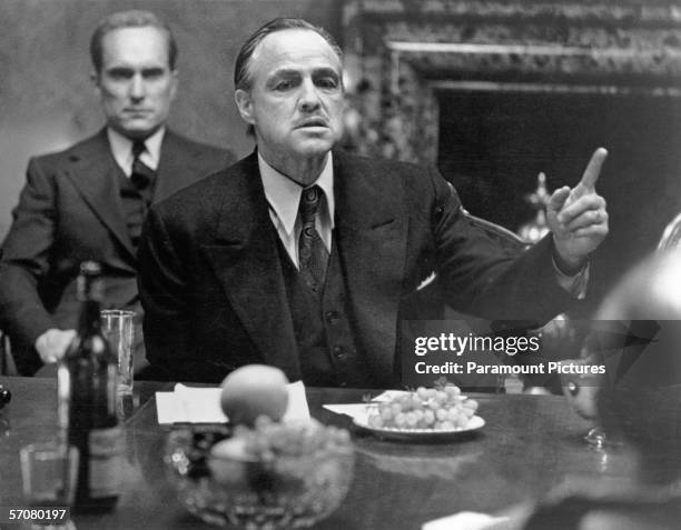 American actor Marlon Brando , in character as mob kingpin Don Vito Corleone, gestures as he sits at a table as colleague and compatriot Robert...