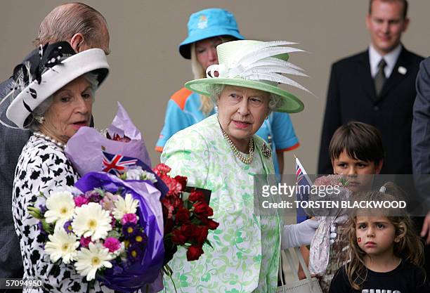 Queen Elizabeth II gives flowers to her lady-in-waiting which she received from two Aboriginal children upon her arrival at the Royal Exhibition...