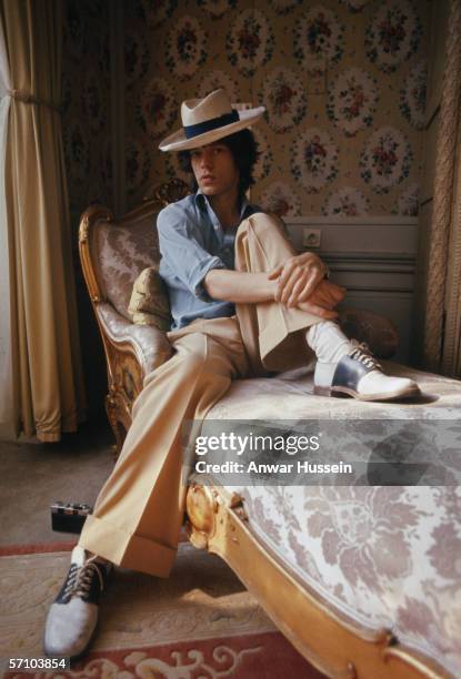 English singer Mick Jagger of the Rolling Stones sitting on a chaise longue in a panama hat and two-tone shoes, October 1973.