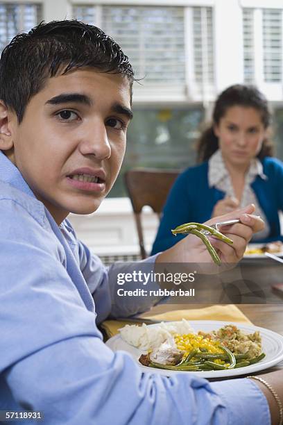 portrait of a teenage boy sitting at a dining table - unangenehmer geschmack stock-fotos und bilder