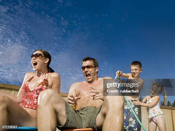 children spraying water on their parents - two kids playing with hose stock pictures, royalty-free photos & images