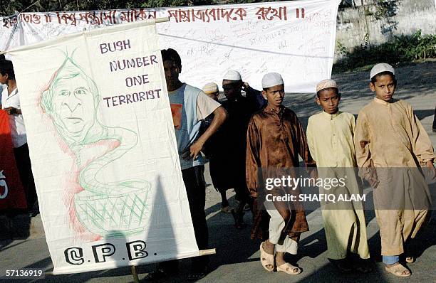An activist from the Bangladesh Communist Party holds a portraits of US President George W. Bush along as Madrasa students walk past during an...