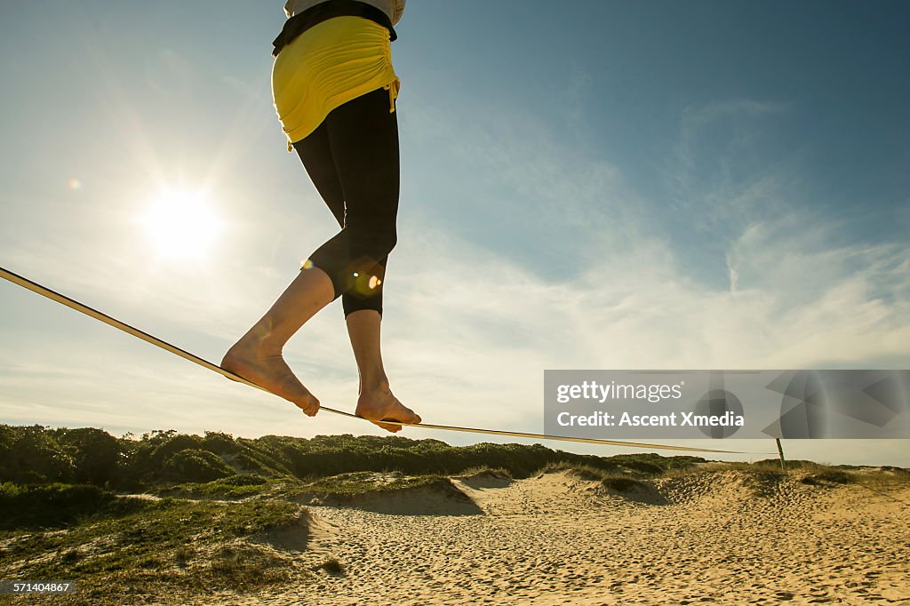 Woman crosses slackline above white sand beach
