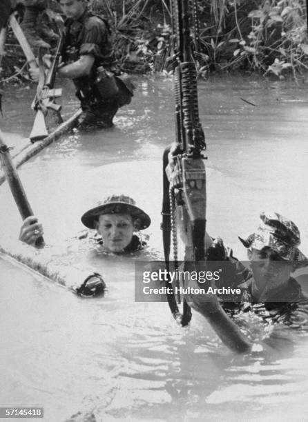 American army combat platoon leader First Lieutenant Alex C. Green and two unidentified soldiers carry weapons as they wade through a deep stream...