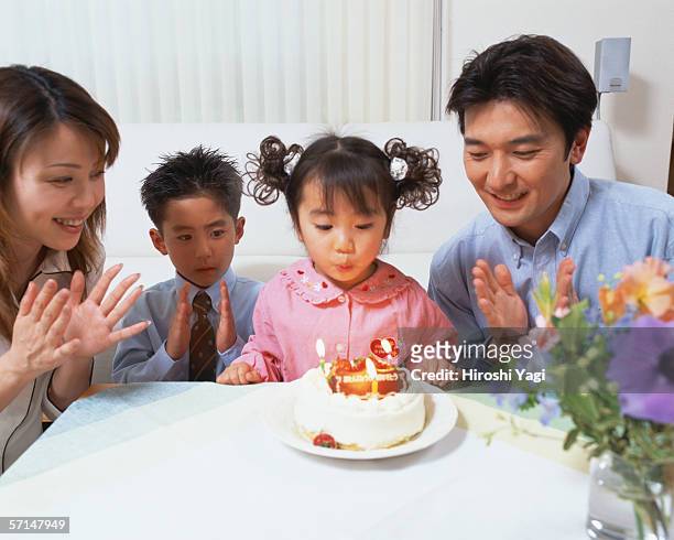a girl blowing out candles on cake and celebrating her birthday with her family - parents children blow candles asians stock pictures, royalty-free photos & images