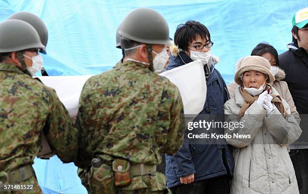 Japan - Relatives watch as members of the Self-Defense Forces carry the coffin of a victim in Higashimatsushima, Miyagi Prefecture, on March 22,...