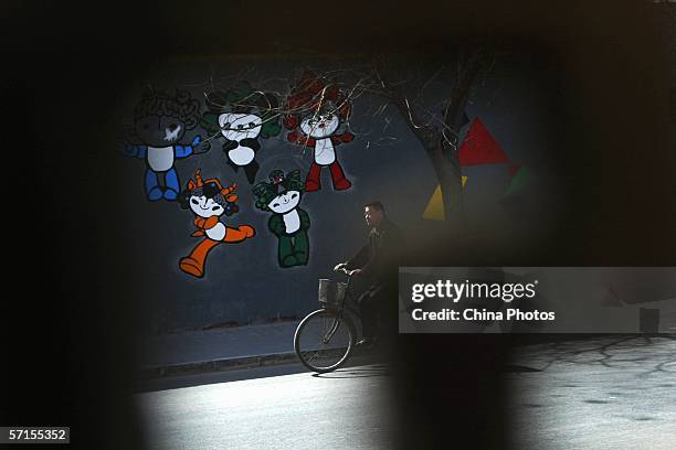 Man rides a bicycle past a wall painted with the five "Fuwas," mascots for the 2008 Olympic Games on March 22, 2006 in Beijing, China. Beijing...