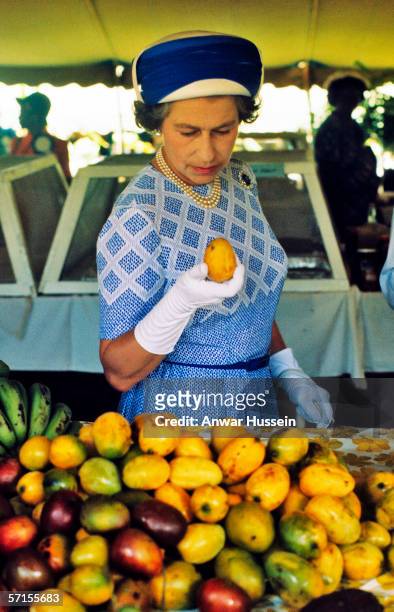 Queen Elizabeth ll picks up a mango as she tours a market in the British Virgin Islands in October of 1977.