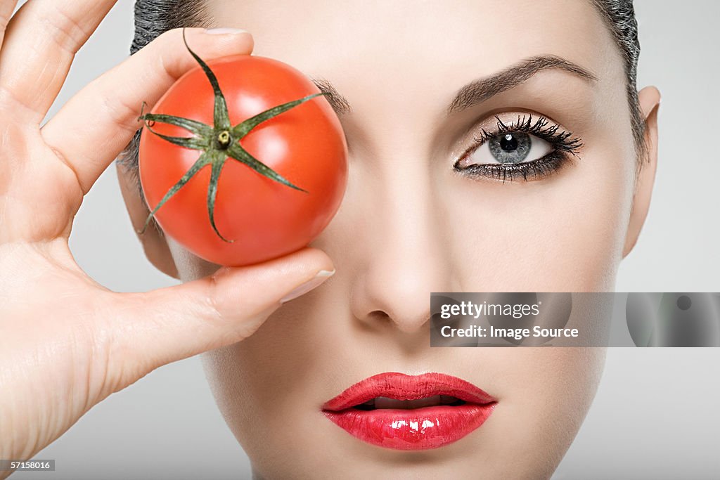 Woman holding tomato over eye