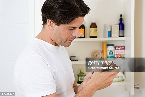 man looking at label on cough medicine - medicine cabinet stock pictures, royalty-free photos & images