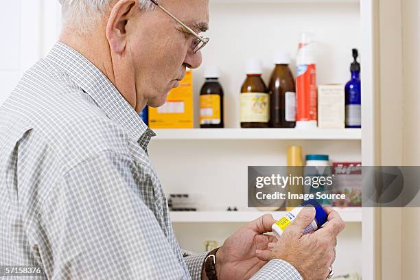 man reading label on bottle of tablets - medicine cabinet stock pictures, royalty-free photos & images