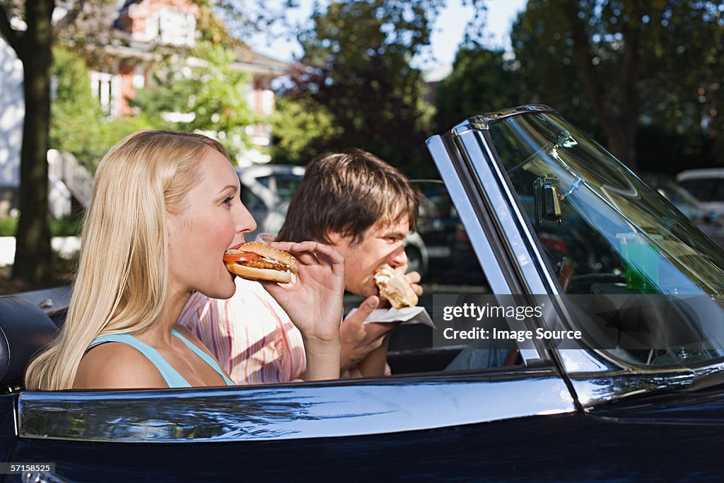 Couple eating burgers in convertible