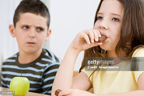 boy looking at girl eating chocolate bar - brother jealous stock pictures, royalty-free photos & images