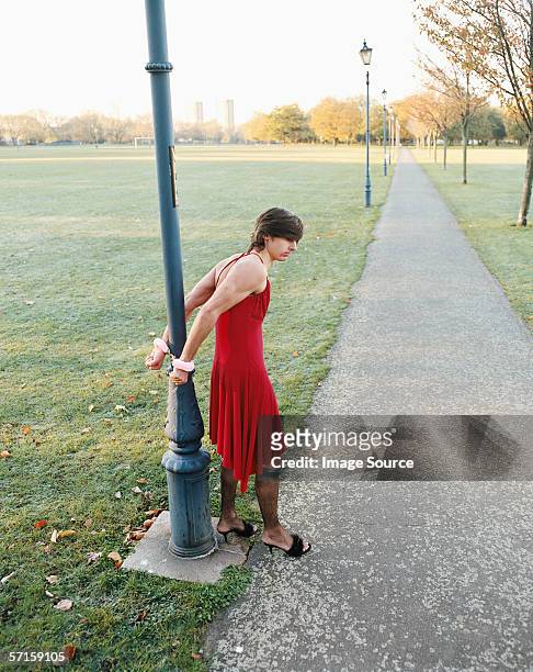 man handcuffed to lamp post wearing red dress - fuzzy handcuffs stock pictures, royalty-free photos & images