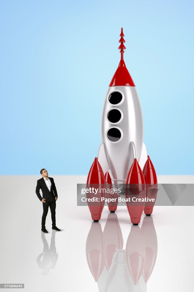 Business man looking at a giant toy rocket ship