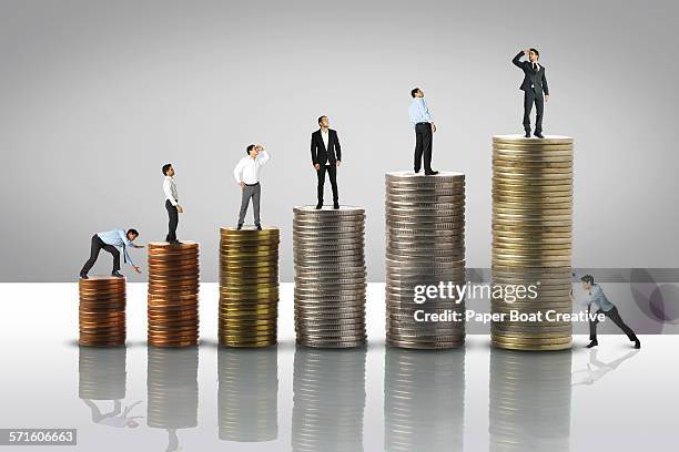 stack of coins from low to high,tiny men on top - busta paga foto e immagini stock