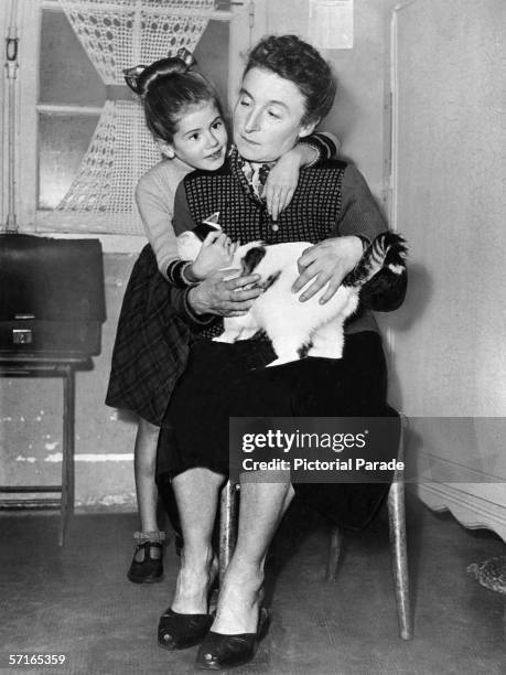 French child poetess Minou Drouet embraces her adopted mother Madame Drouet as they pet a cat, probably in their France home, mid 1950s. Much...