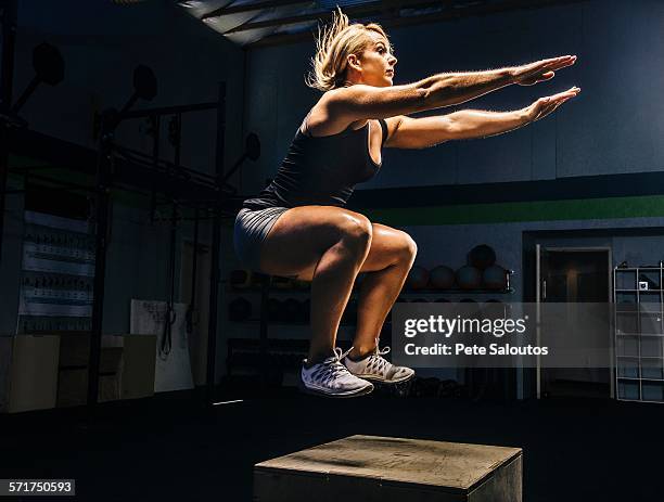 young woman jumping mid air on gym box with arms reaching out - boxing shorts stock-fotos und bilder