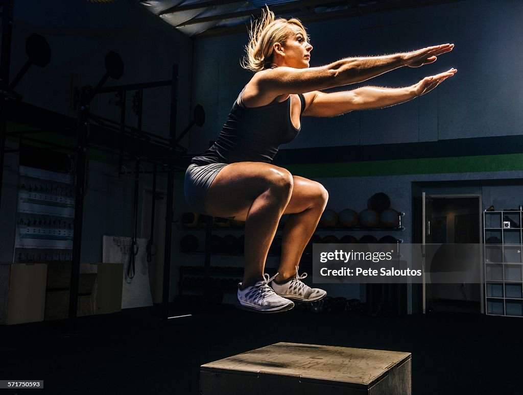 Young woman jumping mid air on gym box with arms reaching out