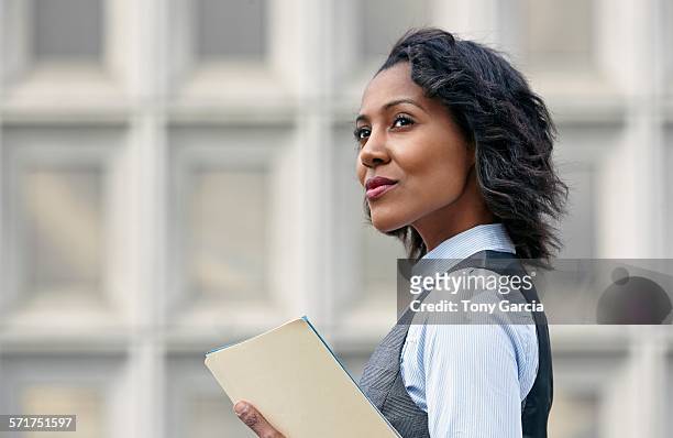 portrait of young business woman holding paper work, looking away, side view - looking away stock-fotos und bilder