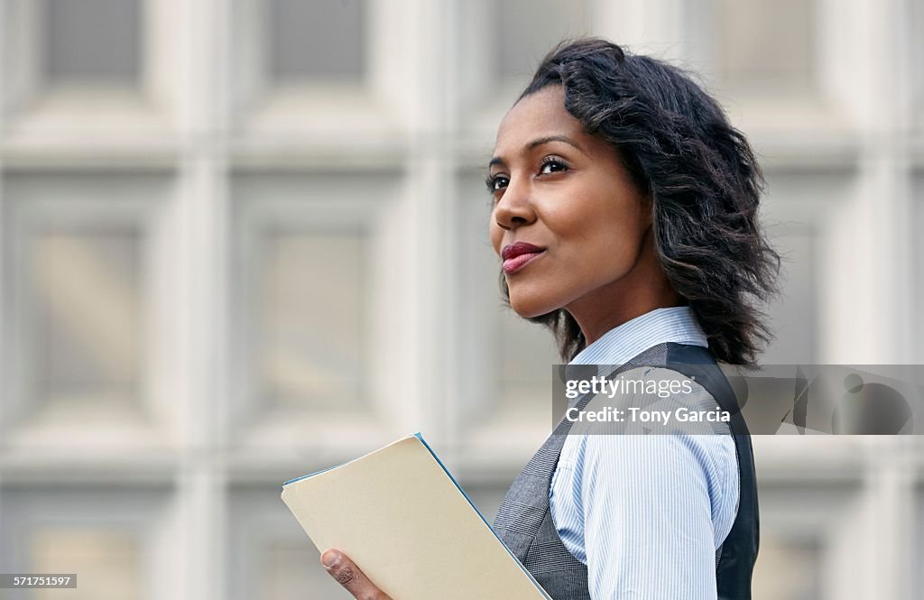 Portrait of young business woman holding paper work, looking away, side view