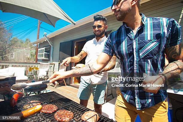 two mid adult brothers barbecuing in garden - barbecue man stock pictures, royalty-free photos & images