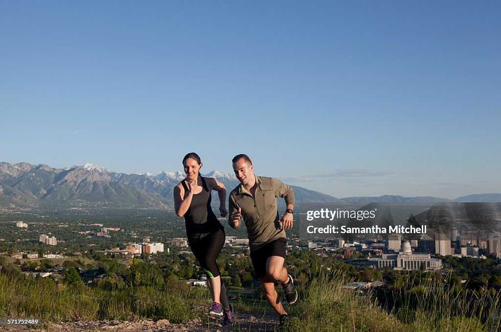 Young female and male runners racing along track above city in valley