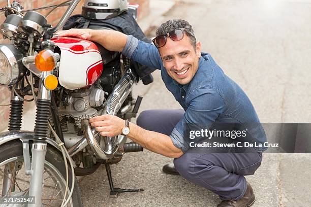 mid adult man crouching beside motorbike - 旁邊 個照片及圖片檔