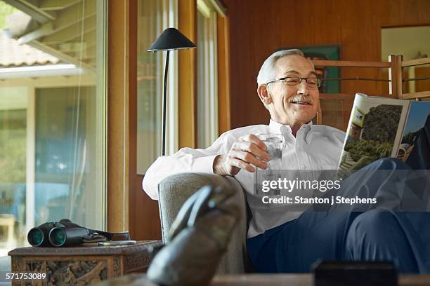 senior man at home, reading magazine - glass magazine stock pictures, royalty-free photos & images