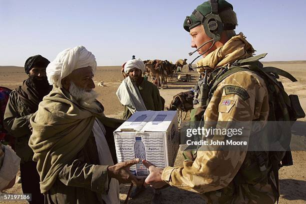 Commando from the 42 Royal Marines gives a case of bottled water to a group of Afghan Kuchi nomads, near Camp Bastion on March 28, 2006 in the desert...