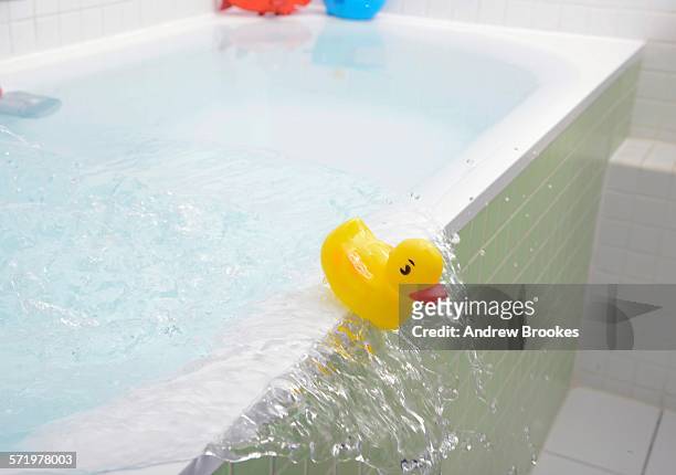 rubber duck falling out of bath overflowing with water - bathtub stock-fotos und bilder