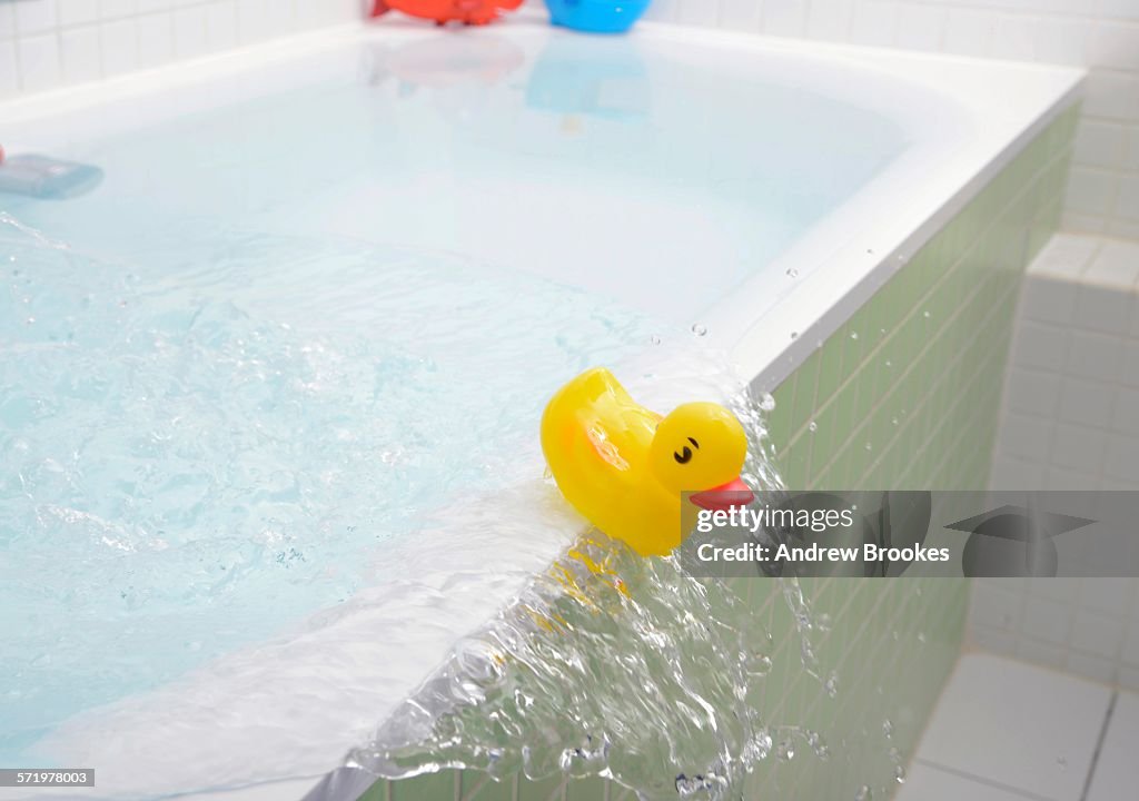 Rubber duck falling out of bath overflowing with water