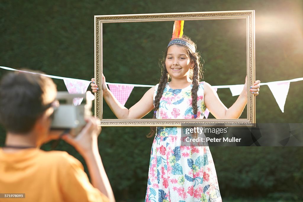 Girl looking through picture frame, having photograph taken