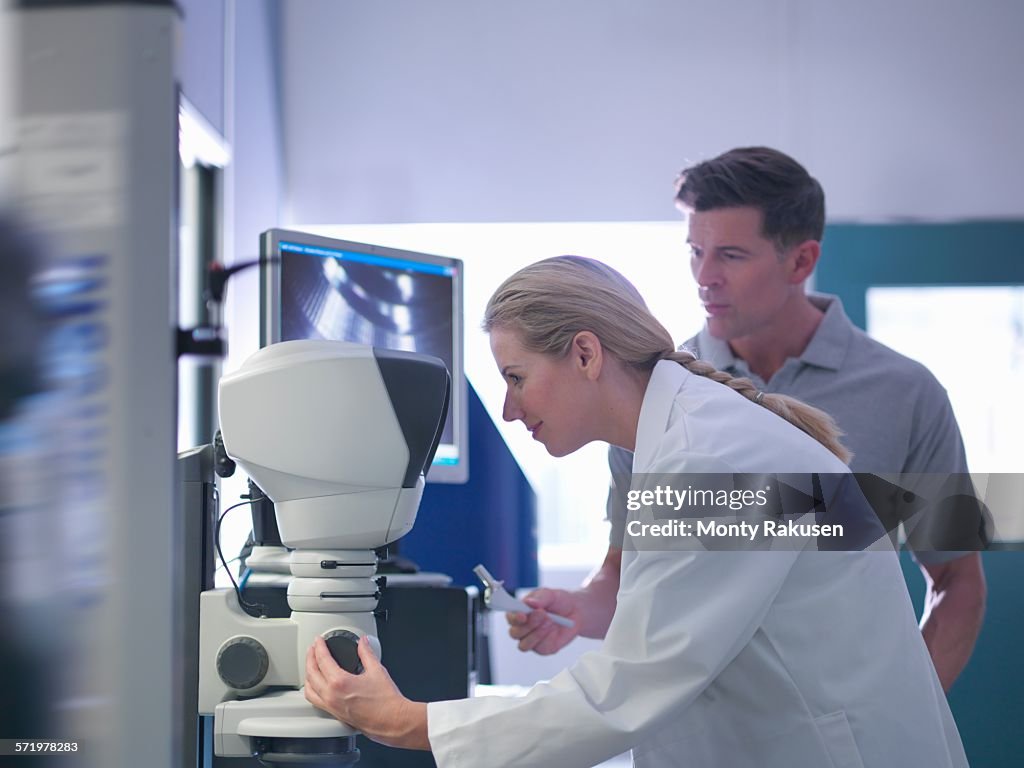 Engineers inspecting artificial hip joint parts using electron microscope in orthopaedic factory